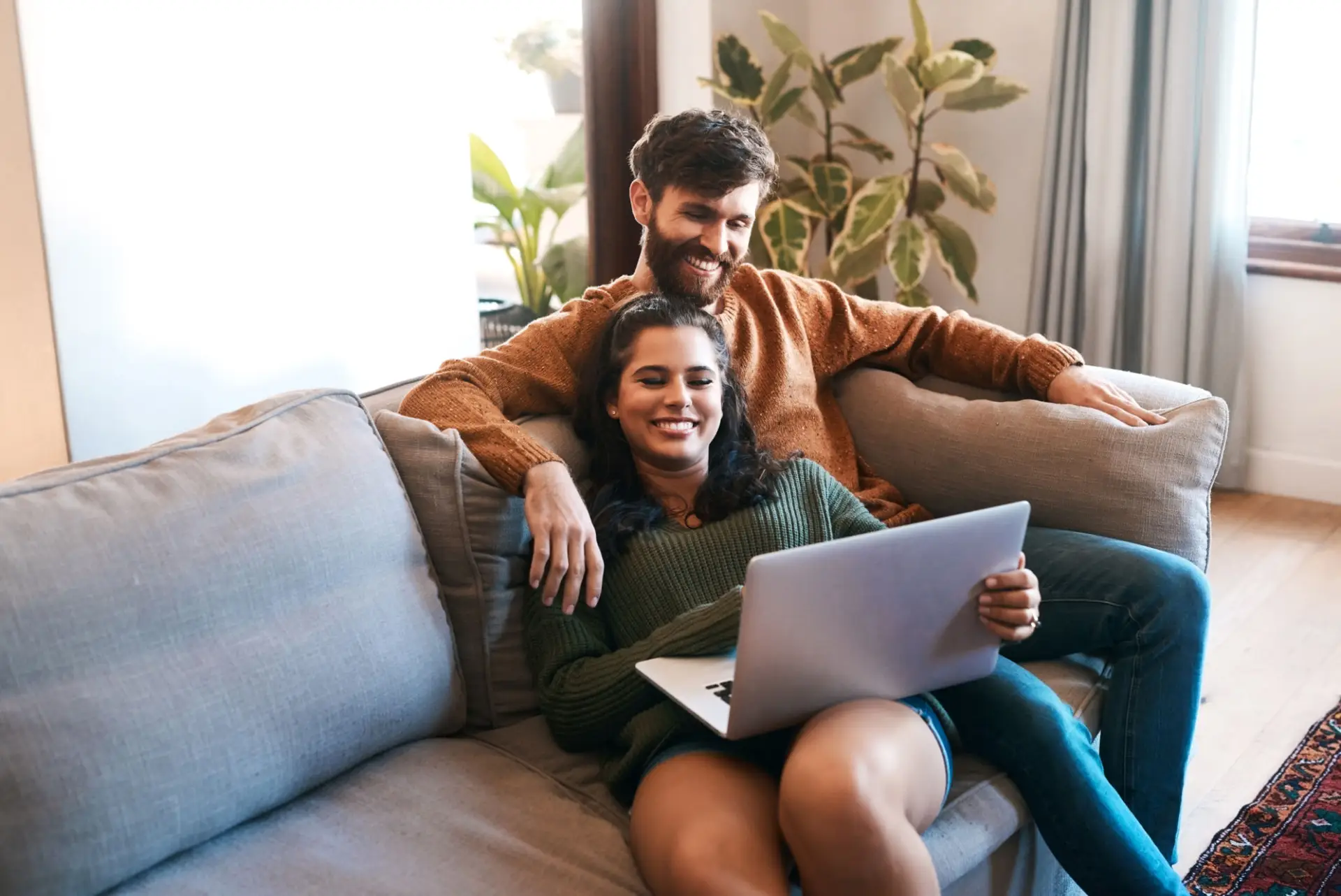 Happy couple on a sofa with a laptop reviewing their mortgage pre approval for a Non Qualified Mortgage Loan at The Wright Loans